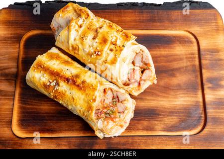 Two golden-brown baked rolls are displayed on a wooden board. Each roll is stuffed with tender chicken and fresh vegetables, showcasing a crispy exter Stock Photo
