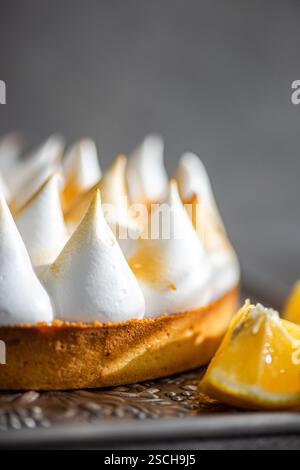 Close up of a a homemade lemon cake showcasing the golden brown peaks of toasted meringue. The dessert rests on a decorative plate with fresh lemon we Stock Photo