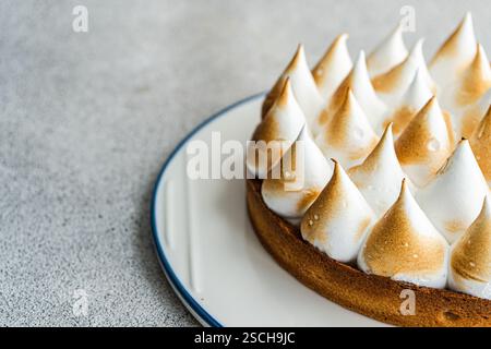 Close up image of a homemade lemon cake, showcasing its golden brown peaks and buttery crust. The dessert is elegantly presented on a white plate agai Stock Photo