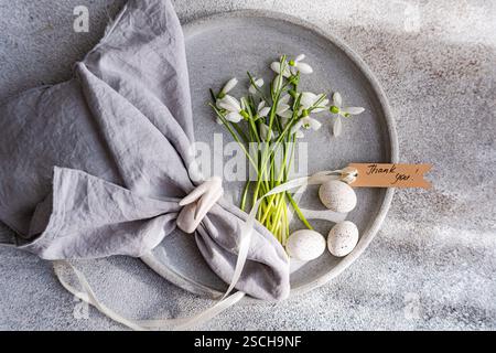 Top view of an exquisite spring table setting featuring fresh snowdrops arranged on a gray ceramic plate, complemented by a gray linen napkin, delicat Stock Photo