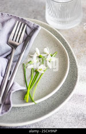Textured grey plate featuring fresh spring snowdrops alongside a fork and a soft cloth napkin, creating a serene dining setup indicative of springtime Stock Photo