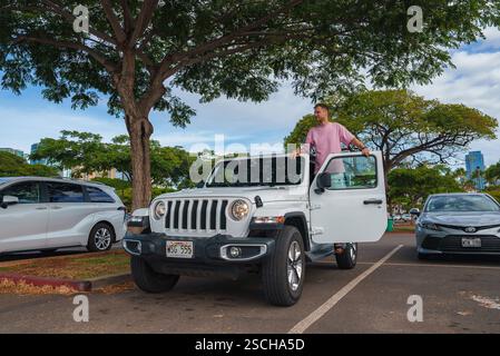 Man Standing on White Jeep Wrangler in Hawaii Parking Lot Stock Photo