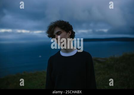 A thoughtful young man with eyes closed stands by the ocean in Signal Hill in St. John's, Newfoundland & Labrador, Canada. And he is lost in contempla Stock Photo
