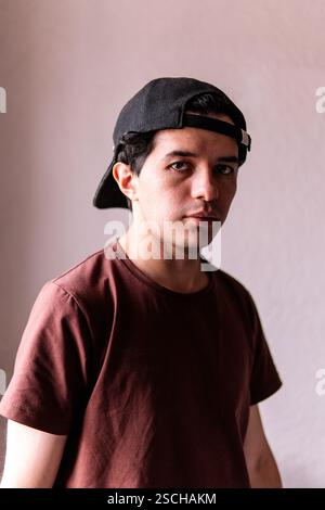 Portrait of a young male wearing a black baseball cap backwards and a maroon t-shirt. He gazes intently at the camera with a focused expression. Stock Photo