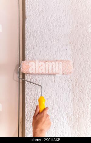 Cropped unrecognizable of a man's hand using a paint roller on a textured wall, capturing a moment of home remodeling. Stock Photo