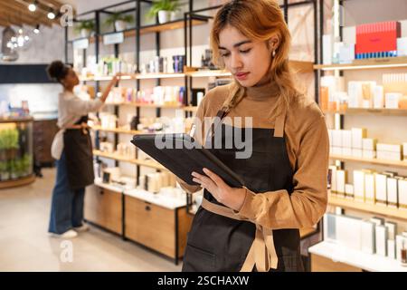 Workers in a cosmetics store are engaged in organizing products on shelves and managing inventory using a tablet. The vibrant setting emphasizes moder Stock Photo