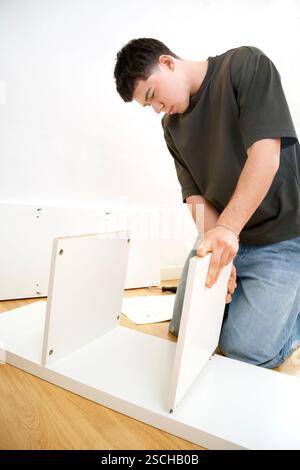 Man carefully assembling new furniture pieces in a well-lit room, focused on fitting together white wooden panels. Stock Photo