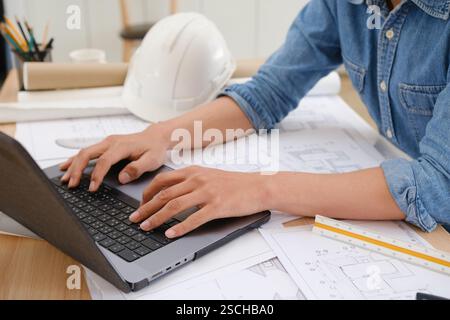 Architect and engineer working on blueprints using a laptop at a desk Stock Photo