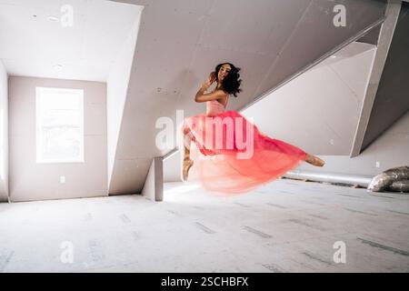 Ballerina in mid-air leap wearing pink tulle dress in bright loft Stock Photo