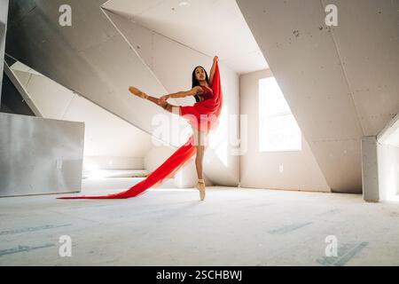 Ballerina in red fabric performing an elegant arabesque in a loft Stock Photo