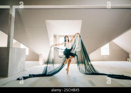 Ballerina in flowing green fabric posing gracefully in a loft space Stock Photo