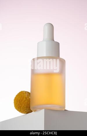 Elegantly displayed cosmetic serum bottle with a dropper, positioned on a geometric podium against a soft pink background, highlighting the product's Stock Photo