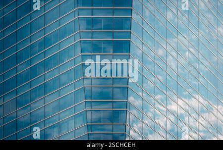 Close-up of a modern glass building facade reflecting a clear blue sky and fluffy clouds, showcasing intricate geometric patterns and lines in a bustl Stock Photo
