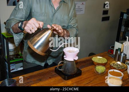 A barista carefully pours hot water into a dripper, crafting specialty coffee with precision. Surrounded by bowls of ingredients, the table showcases Stock Photo