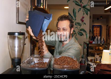 A coffee artisan pours specialty beans into a grinder in a cozy cafe. The setting highlights attention to detail in crafting high-quality coffee exper Stock Photo