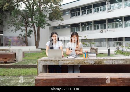 Diverse university students studying together outdoors at a campus table, collaborating on assignments and sharing ideas. Stock Photo