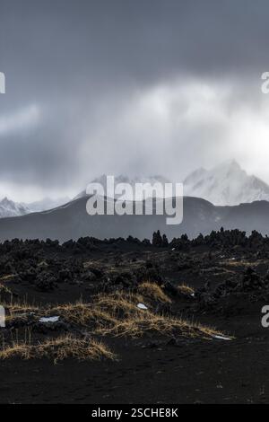 Captivating view of the Icelandic Highlands featuring rugged volcanic terrain, dark rocks, and snow-capped mountains under a dramatic cloudy sky. Stock Photo