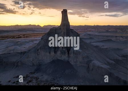 A breathtaking view of the sun setting behind a towering rock formation in the desolate landscape of Utah, USA, highlighting the textured terrain and Stock Photo