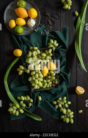 A vibrant display of green grapes, lemons, and limes on a dark wooden surface. The contrasting textures and colors create a fresh and natural composit Stock Photo