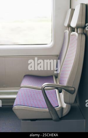 A close up of two empty train seats showing modern design, upholstered in purple fabric with red patterns. The window reveals a blurred view of the mo Stock Photo