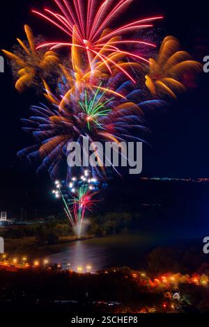 Vibrant fireworks illuminate the night sky above the Ebro River, casting colorful reflections on the water, surrounded by a dark landscape lit by stre Stock Photo