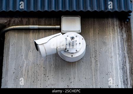 An outdoor surveillance camera, with a robust design, is securely mounted on a corrugated, weathered wall, showing signs of age and exposure to elemen Stock Photo