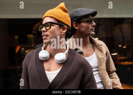 A Colombian gay couple enjoying a relaxed moment together. They wear fashionable clothes, sunglasses, and hats, sitting closely with a sense of camara Stock Photo