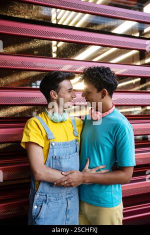 A joyful couple, wearing colorful casual outfits, share a loving moment. They look at each other with smiles, standing against a modern exterior. The Stock Photo