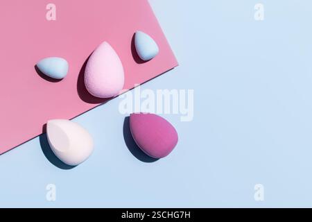 Top view of various colorful makeup egg sponges including pink and blue, arranged artistically on a contrasting pink and blue background Stock Photo