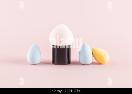 Makeup sponges, also known as beauty blenders, displayed on a soft pink background. The sponge assortment includes shapes and colors such as blue and Stock Photo