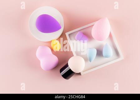 Top view of assorted makeup sponges, including a beauty blender, arranged on a pink background, demonstrating diversity in beauty tools. Stock Photo