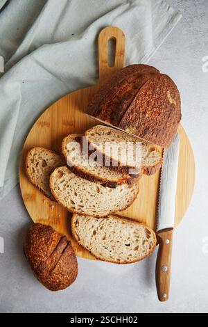 Top view of fresh homemade bread on a wooden cutting board, featuring slices of crusty sourdough bread next to a bread knife and a linen cloth. Stock Photo