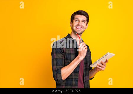 Photo of nice guy with organizer in hands making notes creating startup idea wear casual checkered shirt isolated yellow color background Stock Photo
