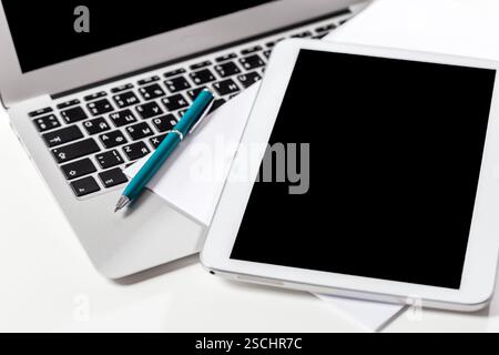 Workspace setup featuring laptop, tablet, pen, and blank sheets for productivity and creativity Stock Photo