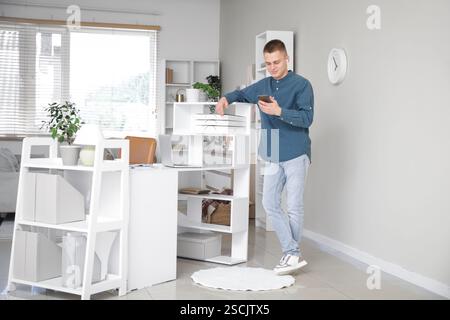 Young male freelancer with mobile phone in light home office Stock Photo