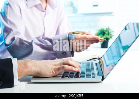 Collaborative work session takes place in a bright office with a laptop and two focused individuals engaging in discussion Stock Photo