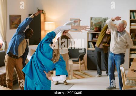 Back view of nurse in blue scrubs doing side bends together with senior people Stock Photo