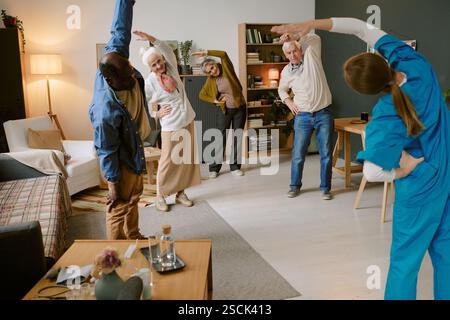 Unrecognizable nurse doing side bends with biracial senior people who standing in circle and repeating after her Stock Photo