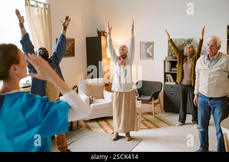 Group of biracial senior people dressed in casual clothes standing in circle and doing morning exercises with unrecognizable young nurse Stock Photo