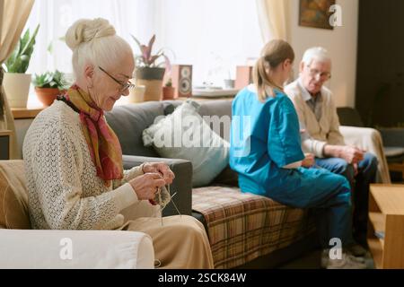 Side view of elegant senior woman wearing glasses while sitting in chair and crocheting Stock Photo