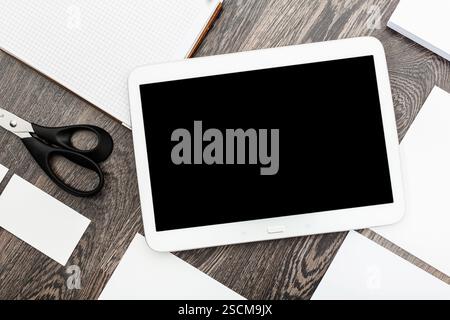 Creative workspace with tablet and stationery on wooden desk featuring various papers and scissors for organizing tasks Stock Photo