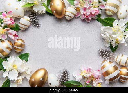 Golden eggs and flowers create a festive easter border on a light background Stock Photo