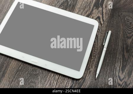 Stylish tablet and pen resting on dark wooden surface, ideal for creative work or note-taking in a modern workspace Stock Photo