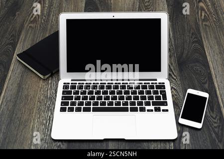 Computing setup with laptop, smartphone, and notebook on a wooden desk featuring a modern workspace Stock Photo