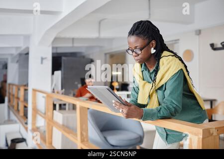 Young woman using digital tablet in contemporary office space with colleagues in background, focusing on task and creating a collaborative environment Stock Photo