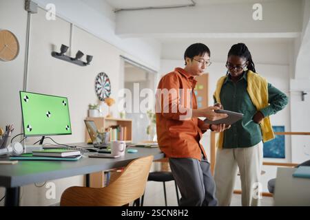 Colleagues discussing project details while using tablet in a bright modern office setting. Both individuals appear engaged and focused on teamwork and productivity Stock Photo