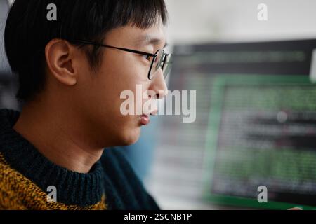 Side profile of a programmer concentrating on computer screen showing lines of code Working in a modern office setting with a blurred background Stock Photo