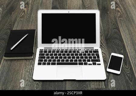 Workspace setup featuring a laptop, smartphone, notebook, and pen on a wooden desk during daylight hours Stock Photo