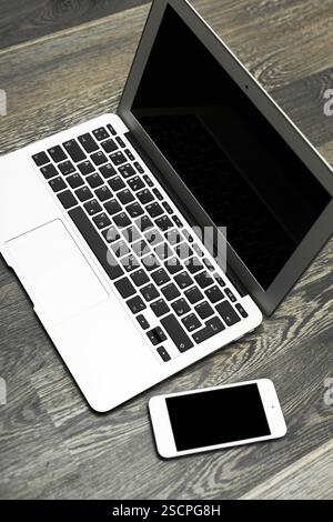 Modern laptop and smartphone placed on a dark wooden table in a minimalistic workspace setting Stock Photo