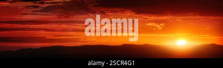 Panorama of a glowing deep orange sunset sky with clouds as vibrant color stripes, in wide banner format Stock Photo
